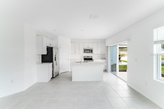 kitchen featuring light tile patterned flooring, appliances with stainless steel finishes, white cabinetry, sink, and a center island with sink