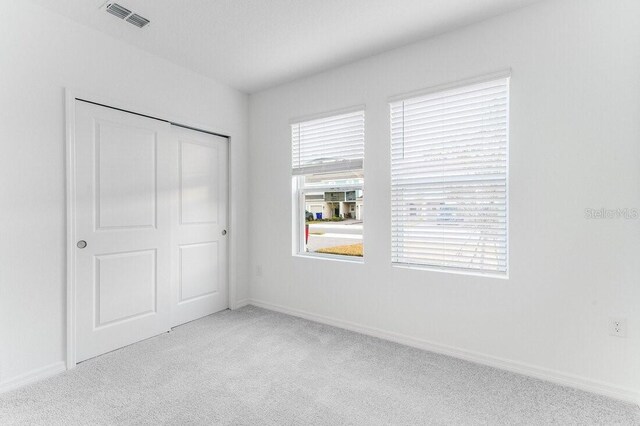 unfurnished bedroom with light colored carpet and a closet