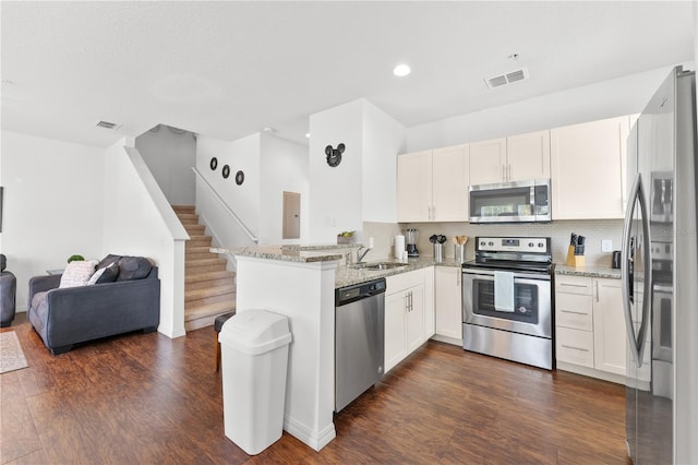 kitchen with light stone counters, kitchen peninsula, dark wood-type flooring, white cabinetry, and stainless steel appliances