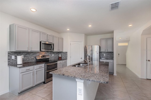 kitchen with sink, tasteful backsplash, gray cabinetry, a kitchen island with sink, and appliances with stainless steel finishes