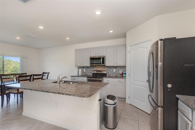 kitchen featuring an island with sink, stainless steel appliances, sink, a breakfast bar area, and backsplash