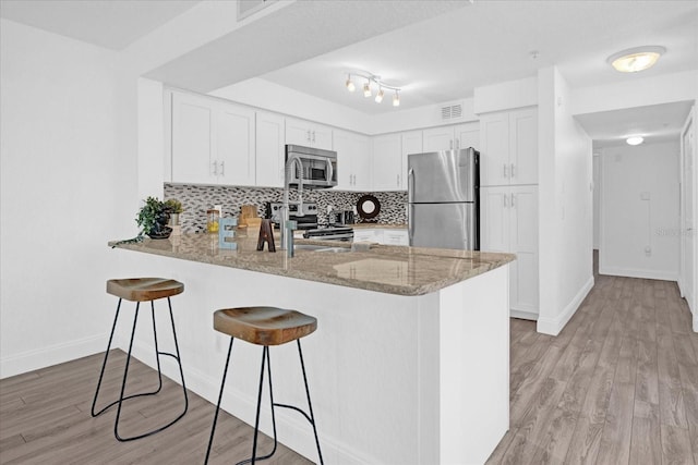 kitchen with appliances with stainless steel finishes, kitchen peninsula, white cabinetry, and light hardwood / wood-style flooring