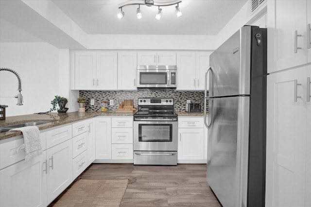 kitchen featuring dark stone counters, white cabinets, appliances with stainless steel finishes, and light hardwood / wood-style flooring