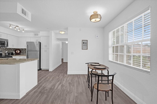 kitchen featuring light stone counters, white cabinets, tasteful backsplash, appliances with stainless steel finishes, and light wood-type flooring