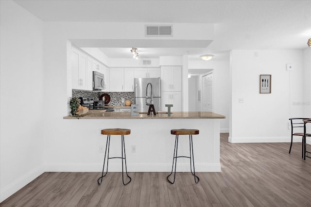 kitchen with kitchen peninsula, white cabinetry, stainless steel appliances, light wood-type flooring, and a kitchen bar