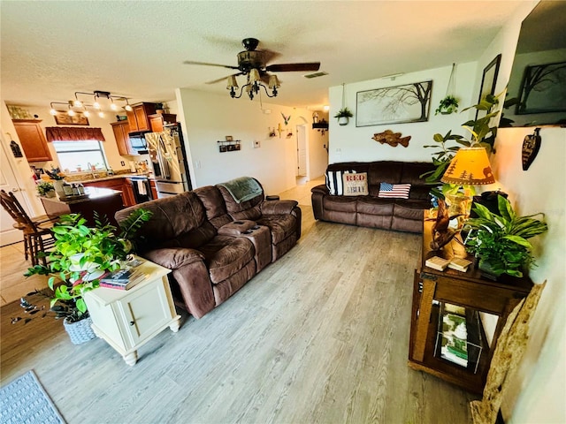 living room featuring light hardwood / wood-style floors, a textured ceiling, and ceiling fan