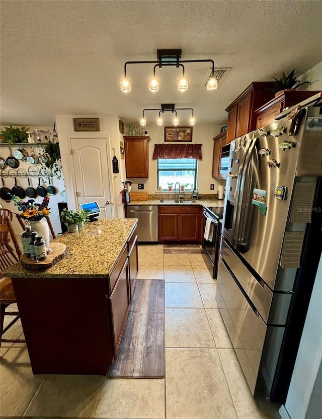 kitchen with a kitchen island, light stone countertops, appliances with stainless steel finishes, light tile patterned floors, and a textured ceiling