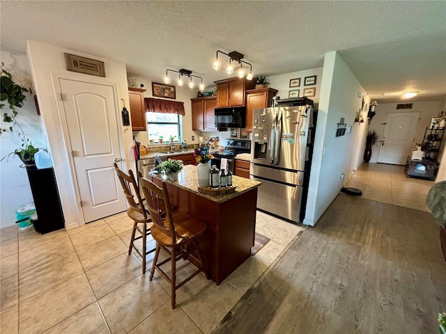 kitchen with a kitchen island, a textured ceiling, appliances with stainless steel finishes, a breakfast bar, and light stone countertops