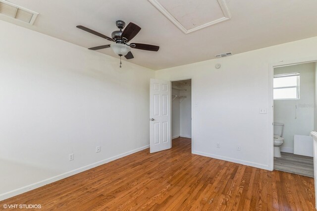 unfurnished bedroom featuring a walk in closet, ceiling fan, wood-type flooring, a closet, and ensuite bath