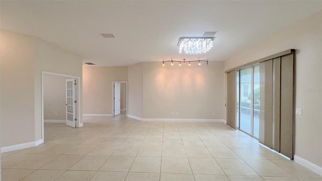 spare room with rail lighting, light tile patterned floors, and an inviting chandelier