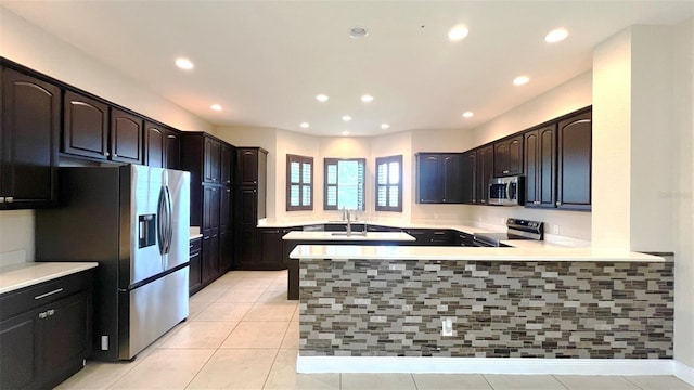 kitchen featuring stainless steel appliances, kitchen peninsula, sink, light tile patterned flooring, and dark brown cabinets