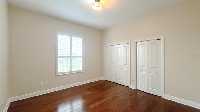 unfurnished bedroom with multiple closets and dark hardwood / wood-style floors