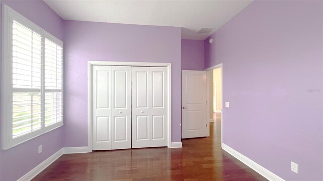 unfurnished bedroom with dark wood-type flooring, multiple windows, and a closet