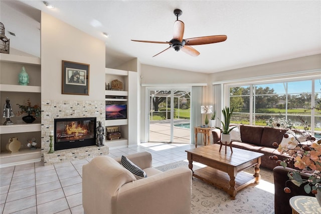 living room with light tile patterned floors, a tile fireplace, ceiling fan, built in shelves, and vaulted ceiling