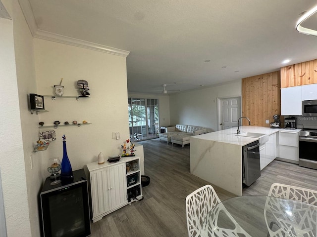 kitchen with dark wood-type flooring, sink, ornamental molding, kitchen peninsula, and appliances with stainless steel finishes