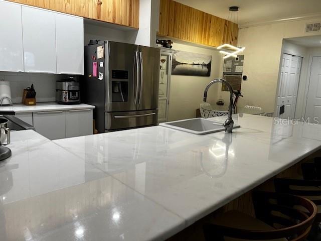 kitchen with pendant lighting, white cabinets, stainless steel refrigerator with ice dispenser, and sink