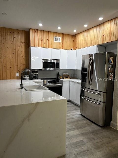 kitchen with sink, kitchen peninsula, white cabinetry, appliances with stainless steel finishes, and light hardwood / wood-style floors