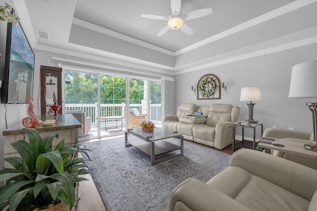 living room featuring ceiling fan, ornamental molding, light wood-type flooring, and a tray ceiling