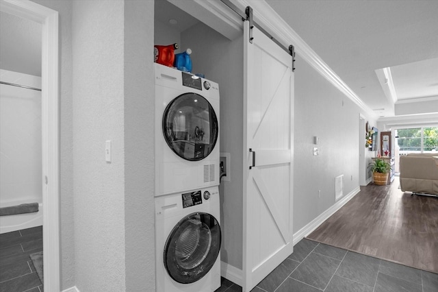 washroom with a barn door, dark hardwood / wood-style floors, stacked washer and clothes dryer, and ornamental molding