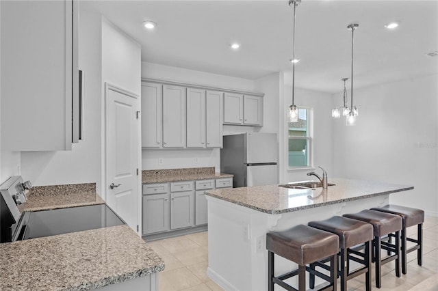 kitchen featuring sink, a kitchen island with sink, light tile patterned flooring, appliances with stainless steel finishes, and decorative light fixtures