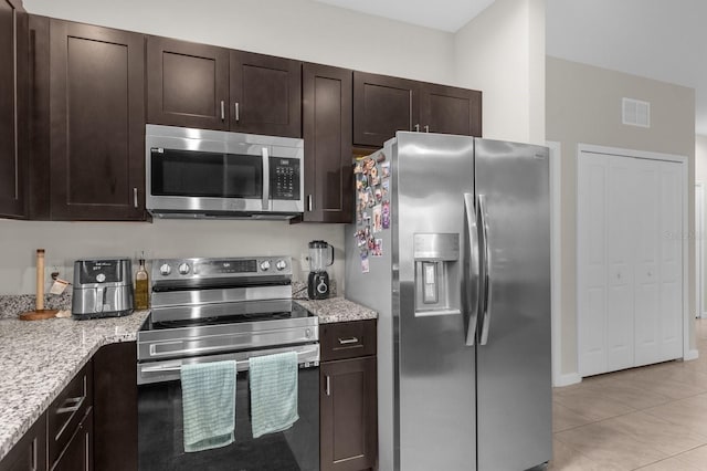 kitchen with appliances with stainless steel finishes, light stone countertops, dark brown cabinets, and light tile patterned floors