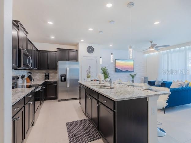 kitchen with pendant lighting, backsplash, sink, an island with sink, and appliances with stainless steel finishes