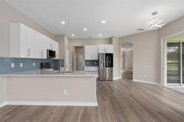 kitchen with light wood-type flooring, pendant lighting, sink, stainless steel appliances, and kitchen peninsula