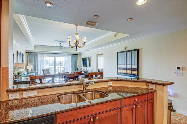 kitchen featuring sink, crown molding, a tray ceiling, and dark stone countertops