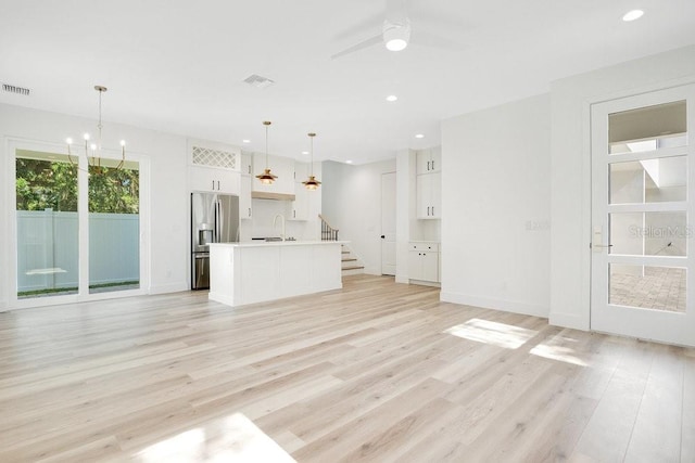 unfurnished living room with ceiling fan with notable chandelier, sink, and light wood-type flooring