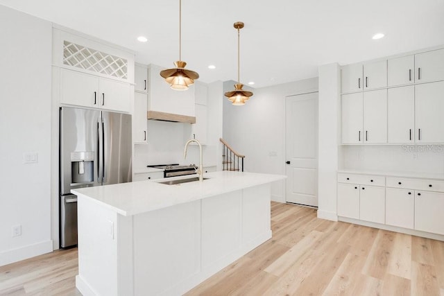 kitchen featuring light wood-type flooring, hanging light fixtures, stainless steel fridge with ice dispenser, an island with sink, and white cabinetry