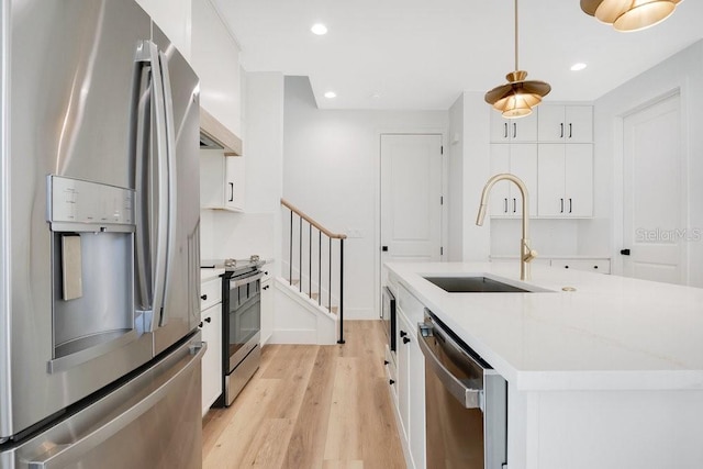 kitchen with white cabinets, stainless steel appliances, hanging light fixtures, and light hardwood / wood-style floors