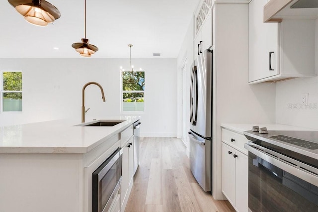 kitchen with light wood-type flooring, hanging light fixtures, white cabinets, and a wealth of natural light