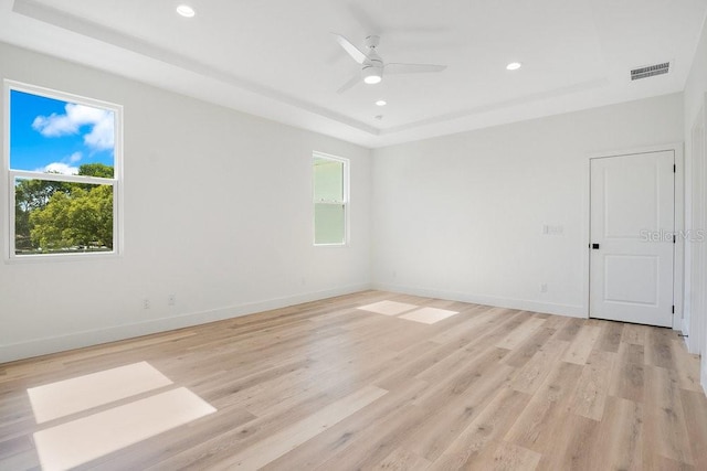 empty room featuring a tray ceiling, light wood-type flooring, and ceiling fan