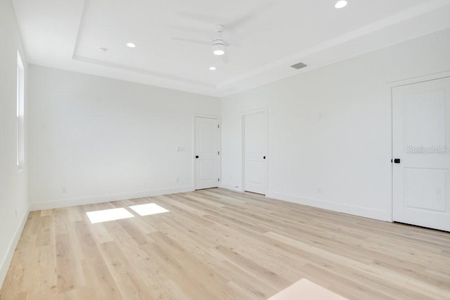 spare room featuring a raised ceiling, light wood-type flooring, and ceiling fan