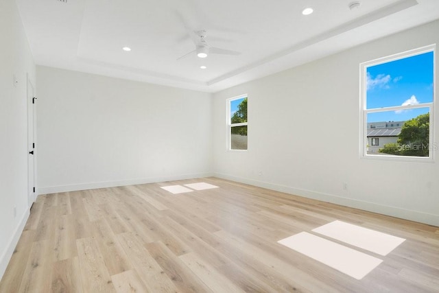 unfurnished room featuring ceiling fan, a tray ceiling, and light hardwood / wood-style floors