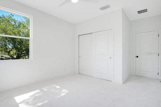 unfurnished bedroom featuring light carpet, a closet, multiple windows, and ceiling fan