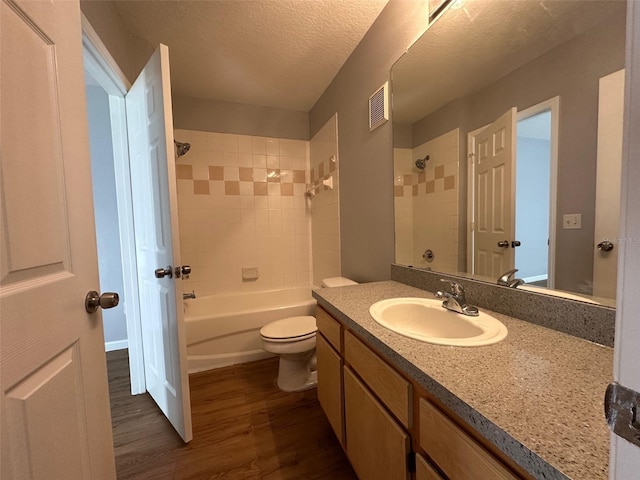 full bathroom featuring tiled shower / bath combo, hardwood / wood-style floors, a textured ceiling, toilet, and vanity