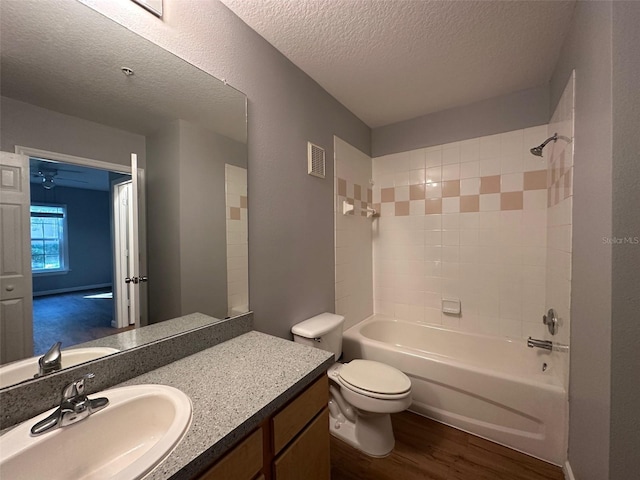 full bathroom with hardwood / wood-style floors, vanity, tiled shower / bath combo, toilet, and a textured ceiling