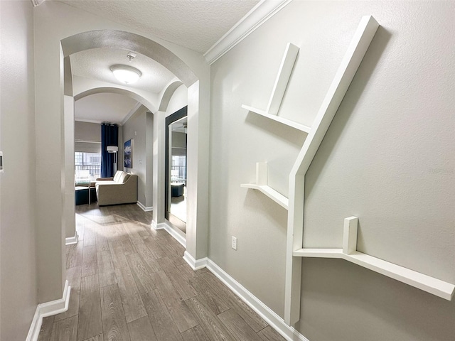 hall featuring crown molding, wood-type flooring, and a textured ceiling