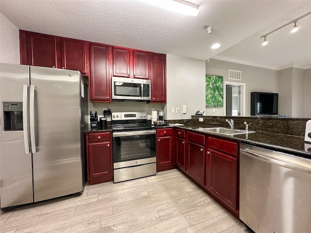 kitchen featuring a textured ceiling, light wood-type flooring, dark stone countertops, sink, and stainless steel appliances