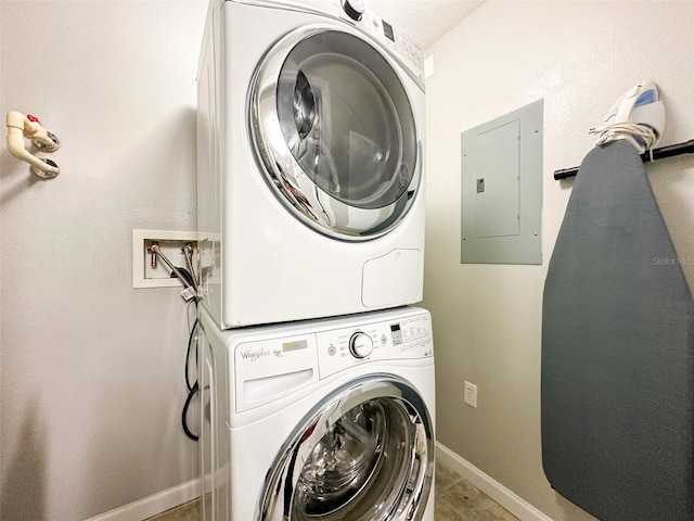 clothes washing area featuring electric panel and stacked washing maching and dryer