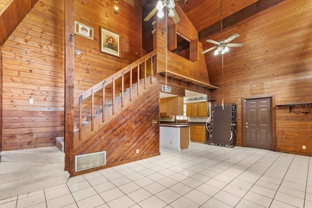 unfurnished living room with wood walls, beam ceiling, light tile patterned flooring, high vaulted ceiling, and ceiling fan