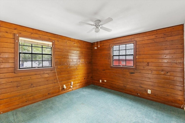 empty room featuring wood walls, ceiling fan, and a wealth of natural light