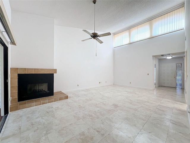 unfurnished living room featuring a textured ceiling, a tiled fireplace, a high ceiling, and ceiling fan