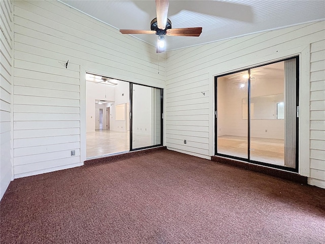 spare room featuring ceiling fan, wooden walls, and dark carpet