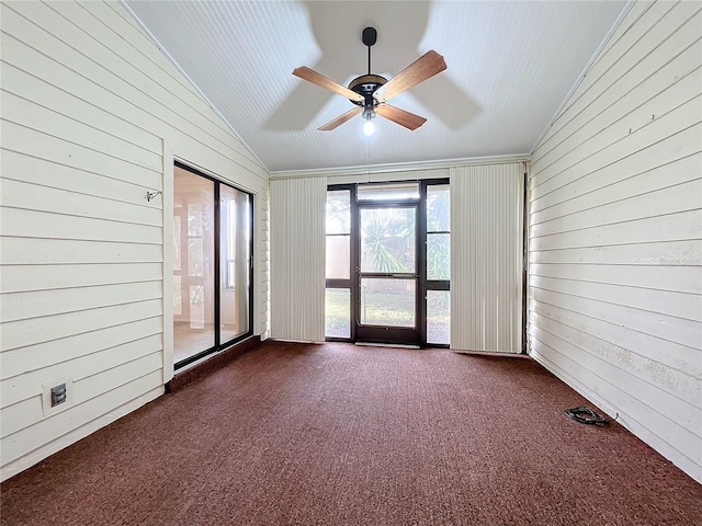 spare room featuring dark carpet, lofted ceiling, wooden walls, and ceiling fan