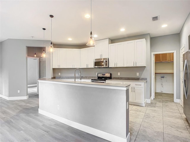 kitchen with white cabinetry, stainless steel appliances, decorative light fixtures, and a kitchen island with sink