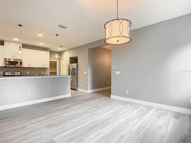 kitchen with white cabinets, light hardwood / wood-style flooring, stainless steel appliances, and decorative light fixtures