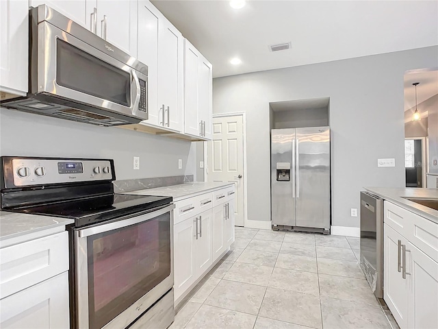 kitchen with appliances with stainless steel finishes, white cabinetry, decorative light fixtures, and light tile patterned floors