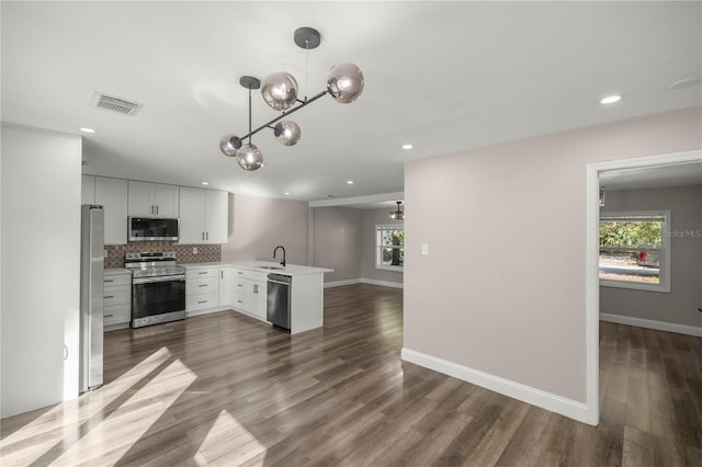 kitchen featuring white cabinets, appliances with stainless steel finishes, dark wood-type flooring, and decorative light fixtures